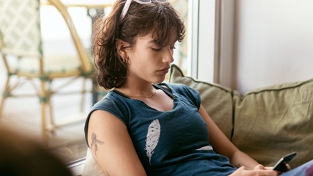 Ung kvinde i sofa med mobiltelefon i gang med at investere