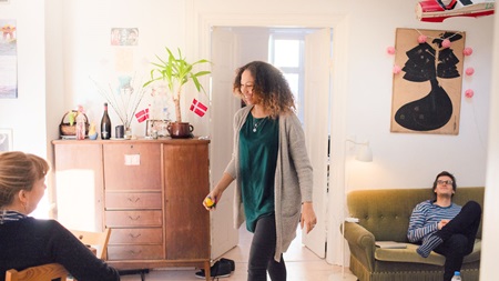 Young girl smiling in living room with roomates Læs om mulighederne med leje-, eje- og andelsboliger, inden du kaster dig ud på boligmarkedet.